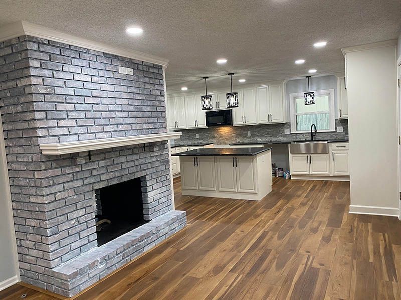 A living room with a fireplace and a kitchen in the background.