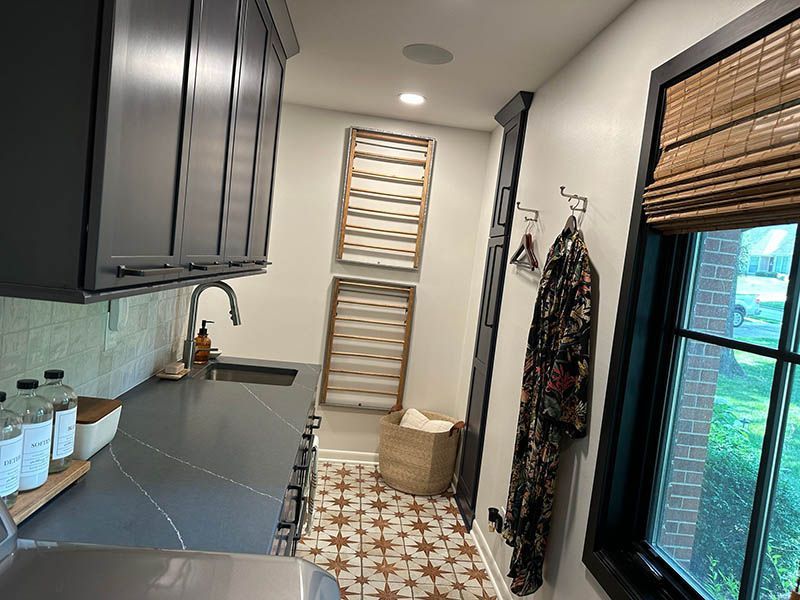 A laundry room with black cabinets , a sink , and a window.