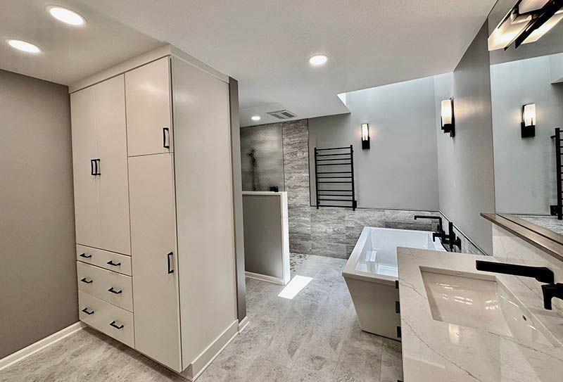 A bathroom with a tub , sink , mirror and cabinets.