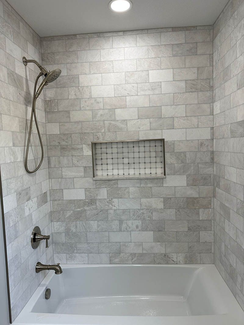 A bathroom with a bathtub , shower , and tiled walls.