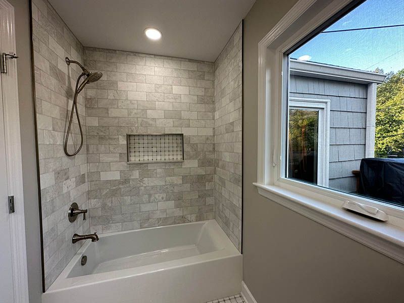 A bathroom with a tub , shower , and window.