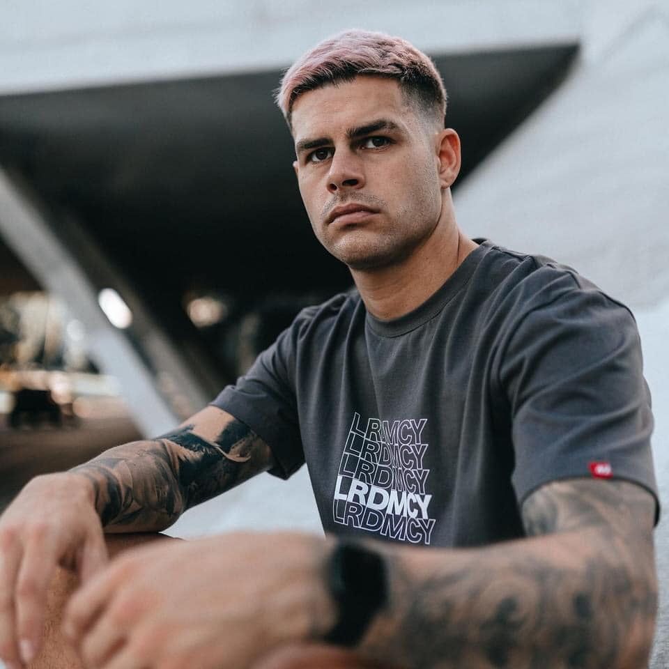 A Man With Tattoos On His Arms Is Wearing A Lrdmcy T-shirt — Carnival Clothing In Miami, QLD