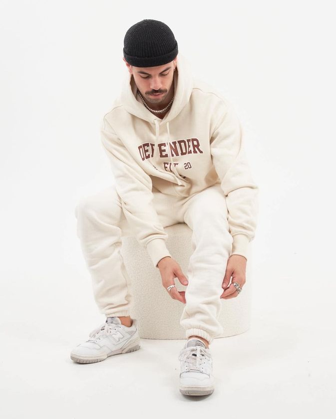 A Man Wearing A White Hoodie And White Sweatpants Is Sitting On A White Block — Carnival Clothing In Miami, QLD
