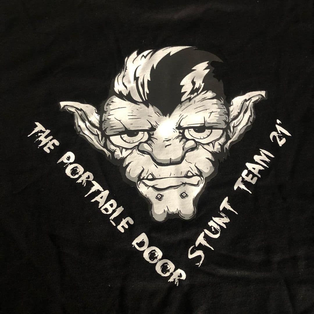 A Black Shirt With A Troll On It That Says The Portable Door Stunt Team 21 — Carnival Clothing In Miami, QLD