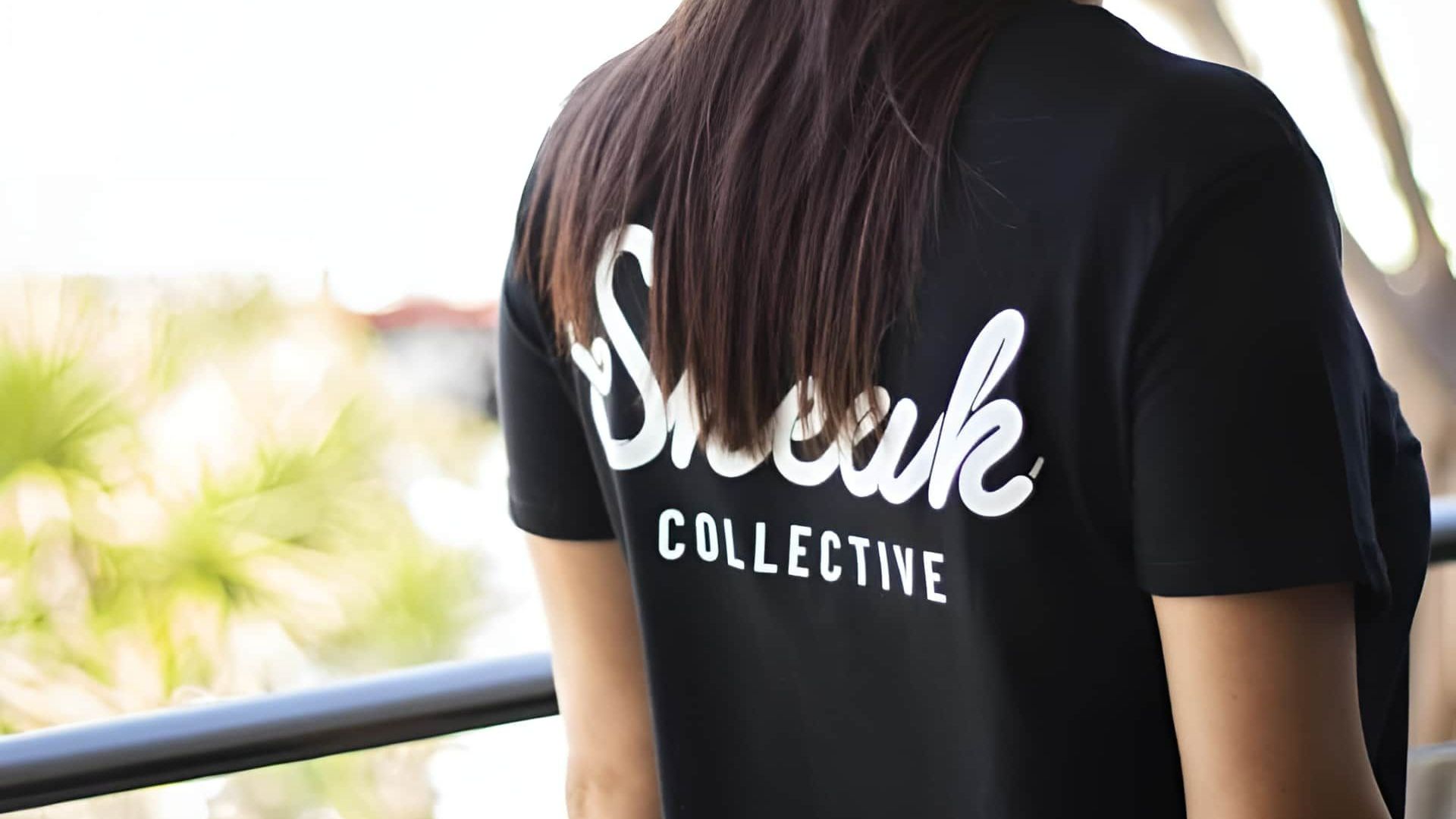 A Woman Is Wearing A Black T-shirt With The Word Sneak Collective On The Back — Carnival Clothing In Miami, QLD