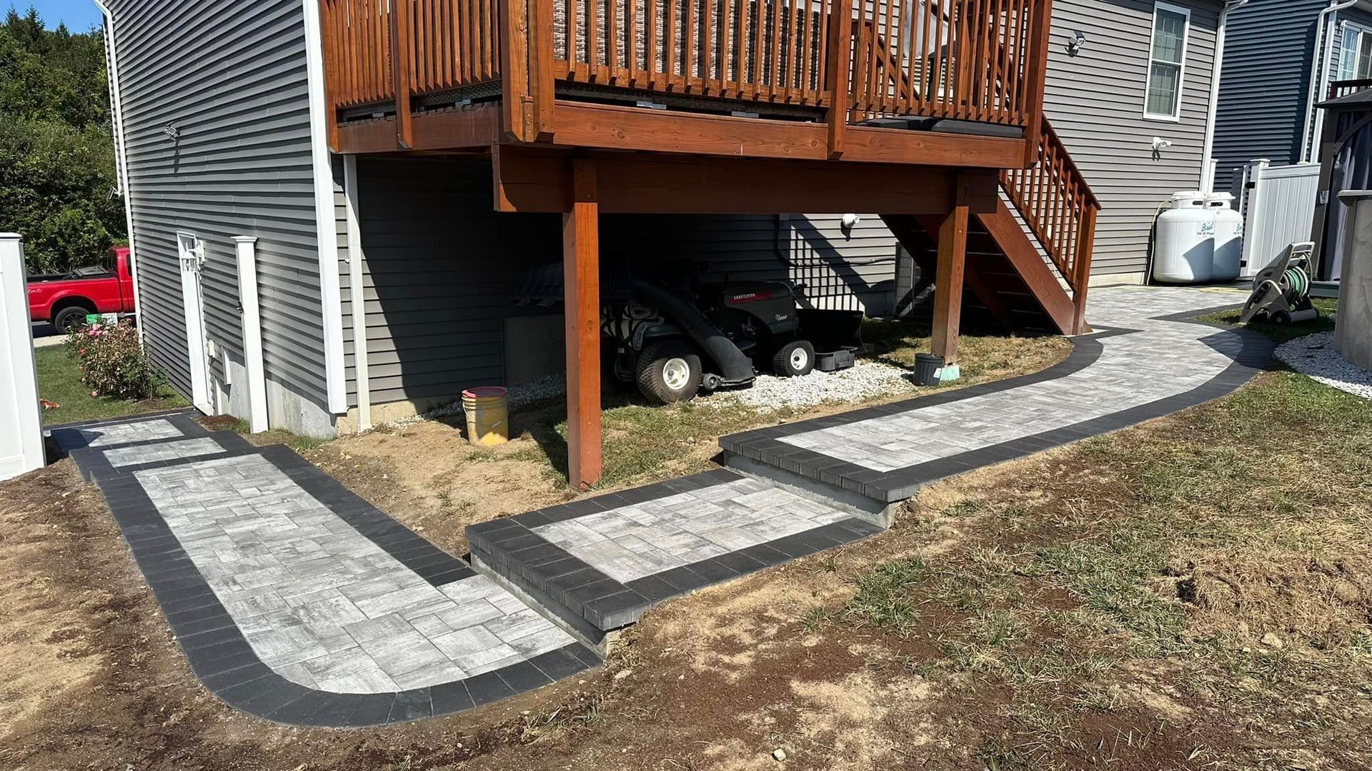 Pathway of gray pavers with black border leads to a wooden deck and stairs.