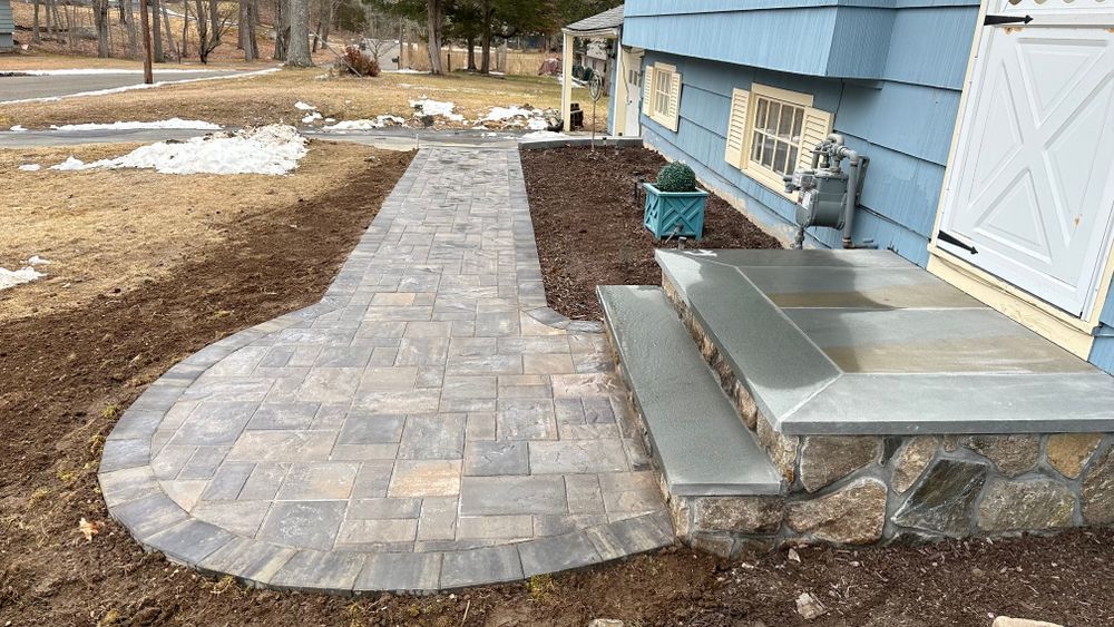 Stone paver walkway and steps leading to a light blue house, surrounded by dirt and mulch.