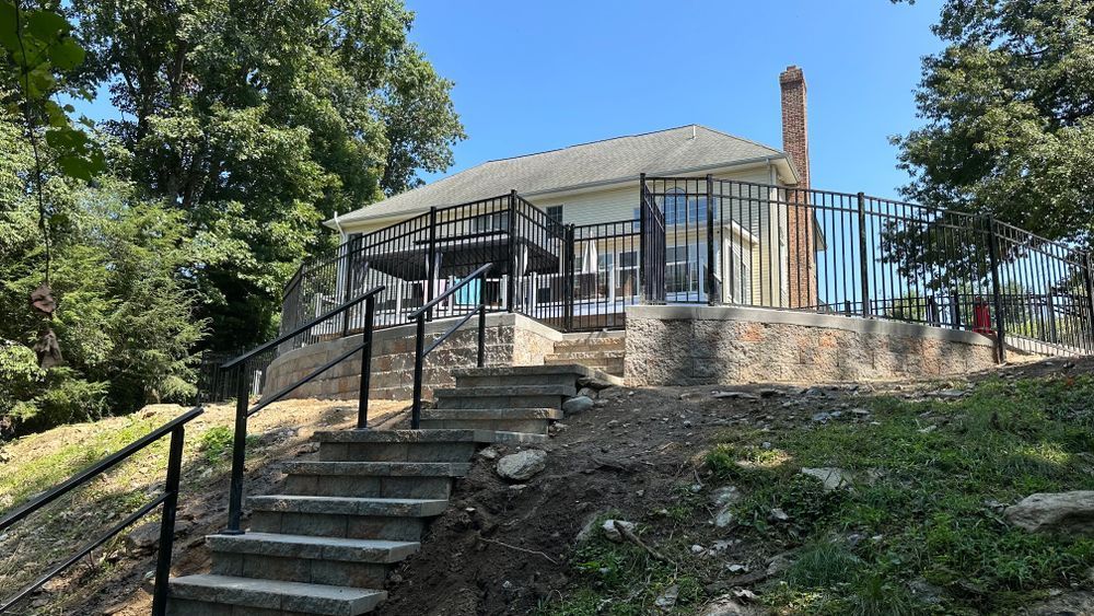 A stone staircase leads up to a white house with a black fence and chimney on a sunny day.