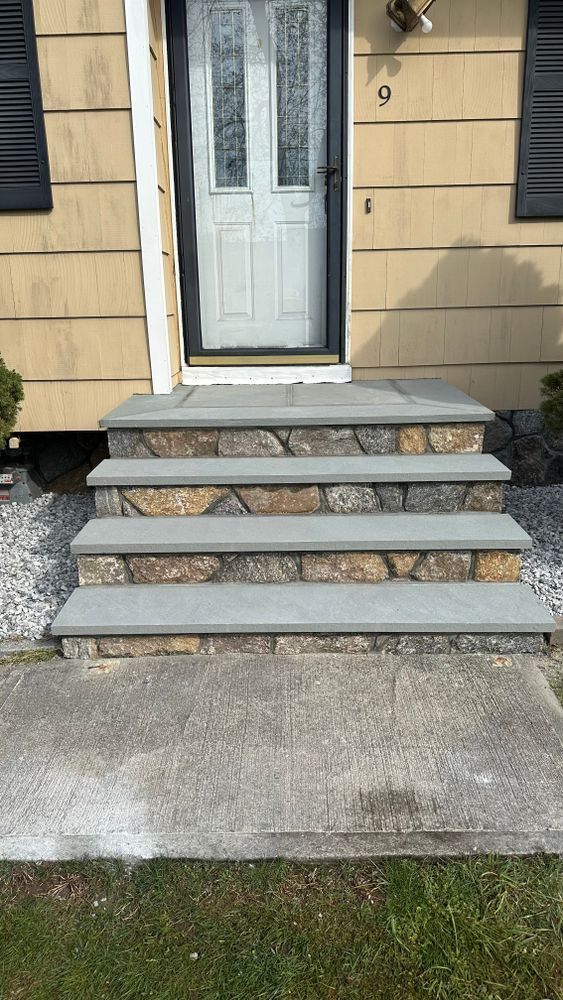 Stone steps leading up to a house door, with a concrete slab at the bottom. Gray and brown stones are used throughout.