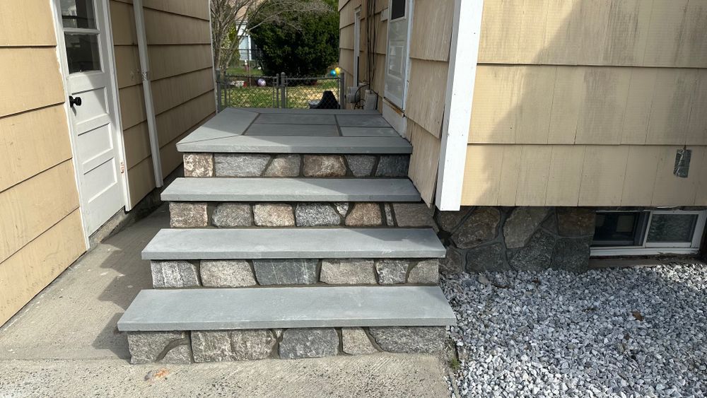 Stone steps leading to a front door, with a small landing. The steps have a gray stone top and a stacked stone facade.