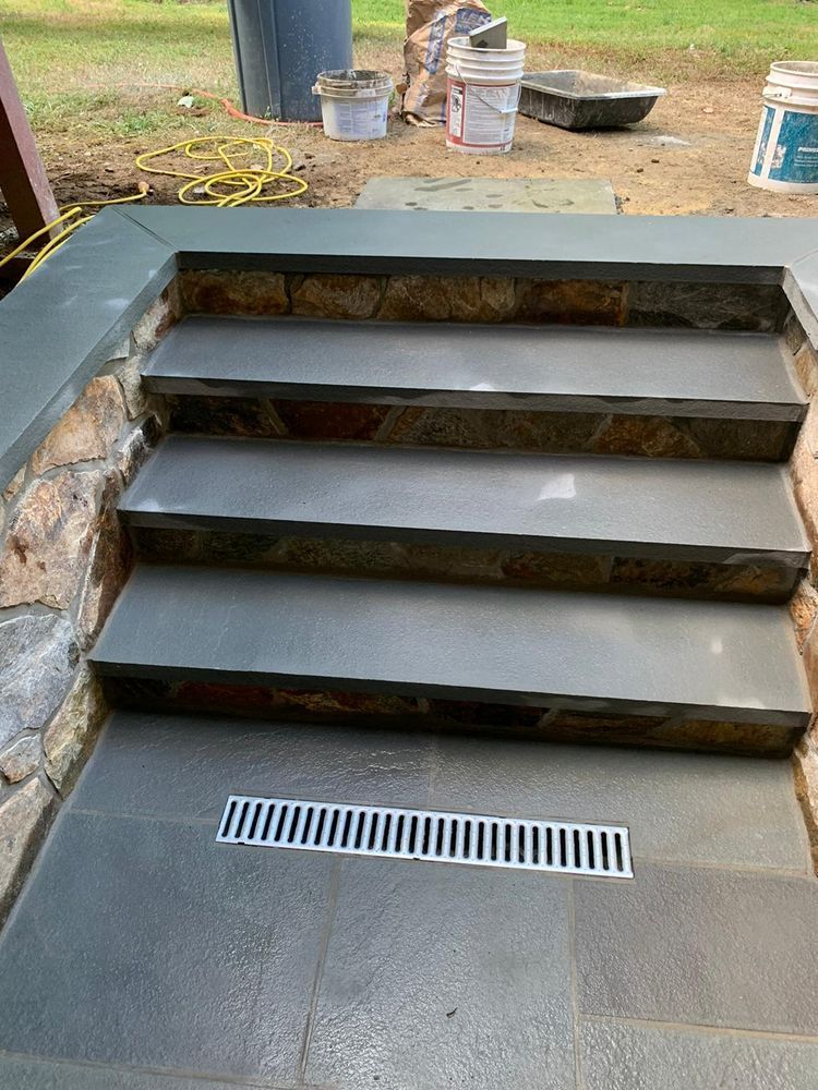Stone steps with a drainage grate at the bottom, leading up to a patio area, with stone and brickwork visible.