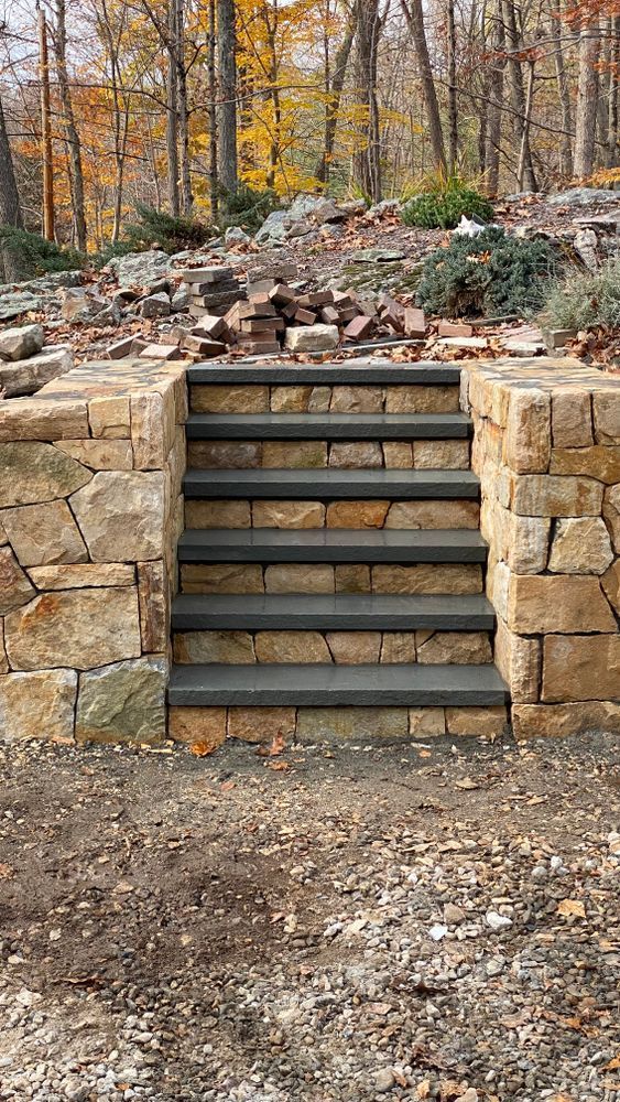 Stone steps built into a rock wall, leading up to a hillside with fall foliage.