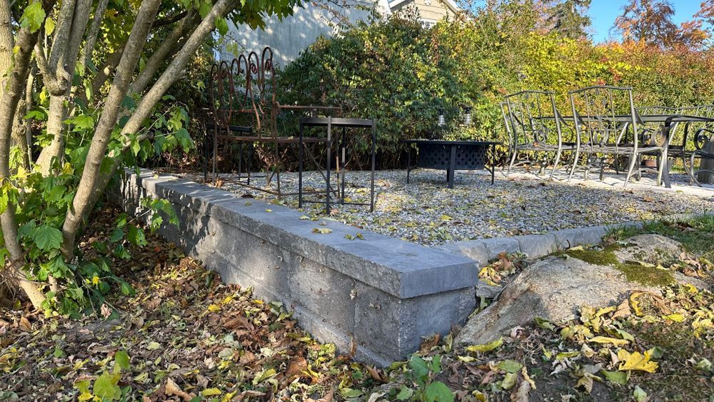 A raised gravel garden bed with a low concrete wall, featuring a weathered metal frame and surrounding foliage.