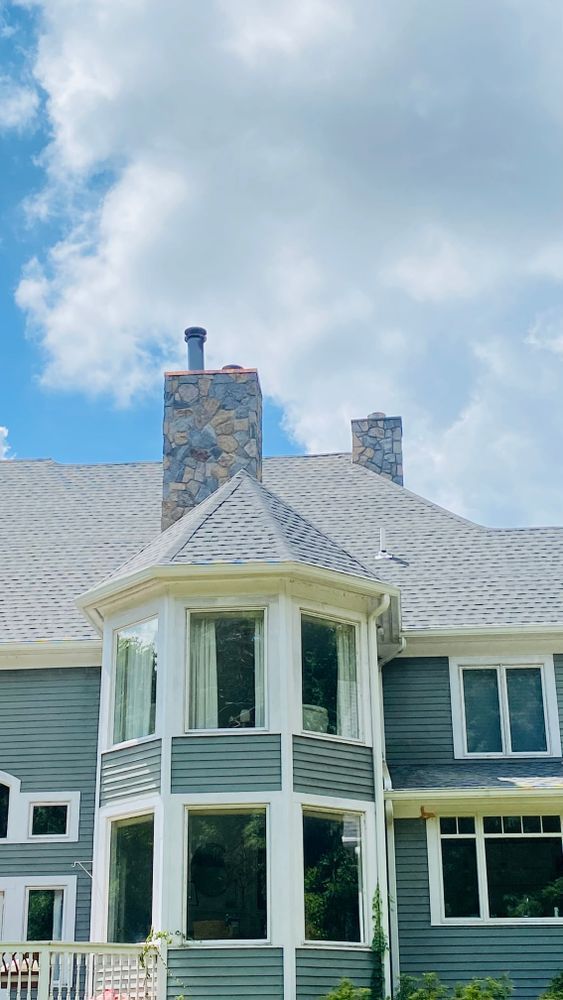 A light blue house with a stone chimney and bay windows against a cloudy sky.