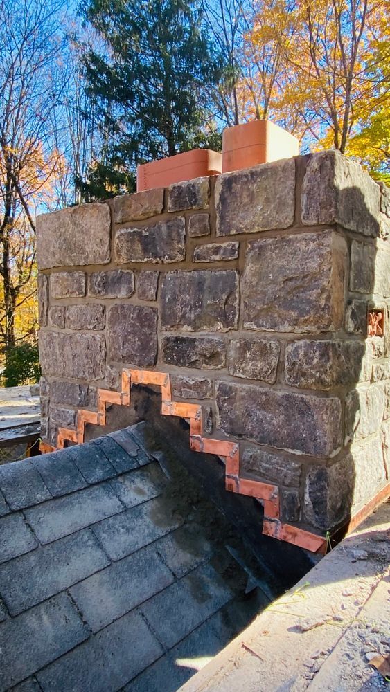 A stone chimney with a red brick zig-zag pattern near the roof. The autumn trees and blue sky are in the background.