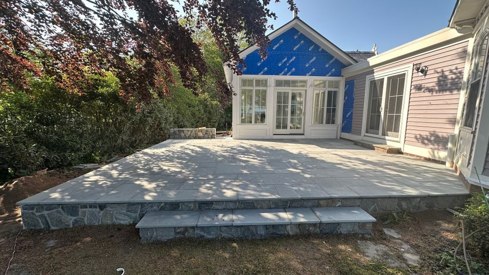 A gray stone patio with steps in front of a house. The house features a blue-covered wall and white-framed glass doors.