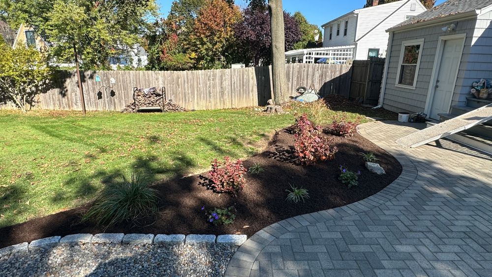 Backyard with a brick patio, landscaped garden beds, and a wooden fence.