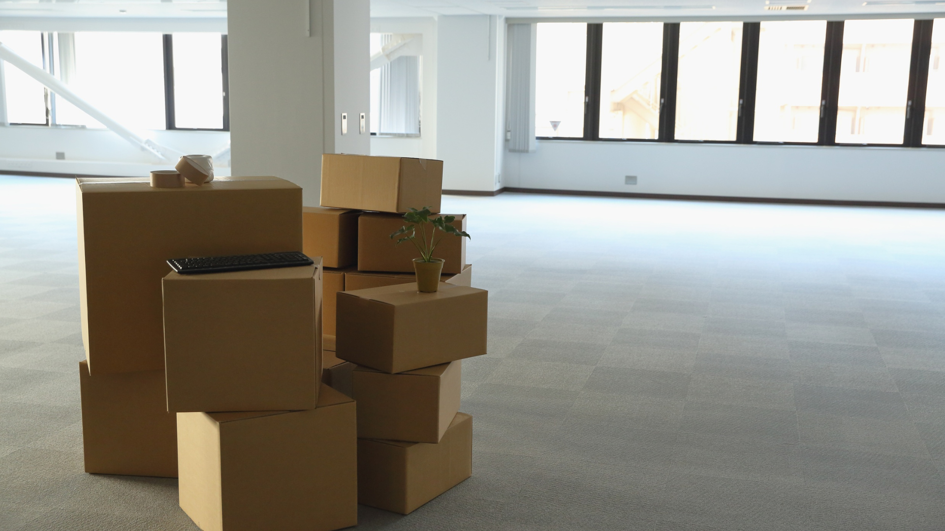 Cardboard boxes stacked in an empty, bright office space near a large window.