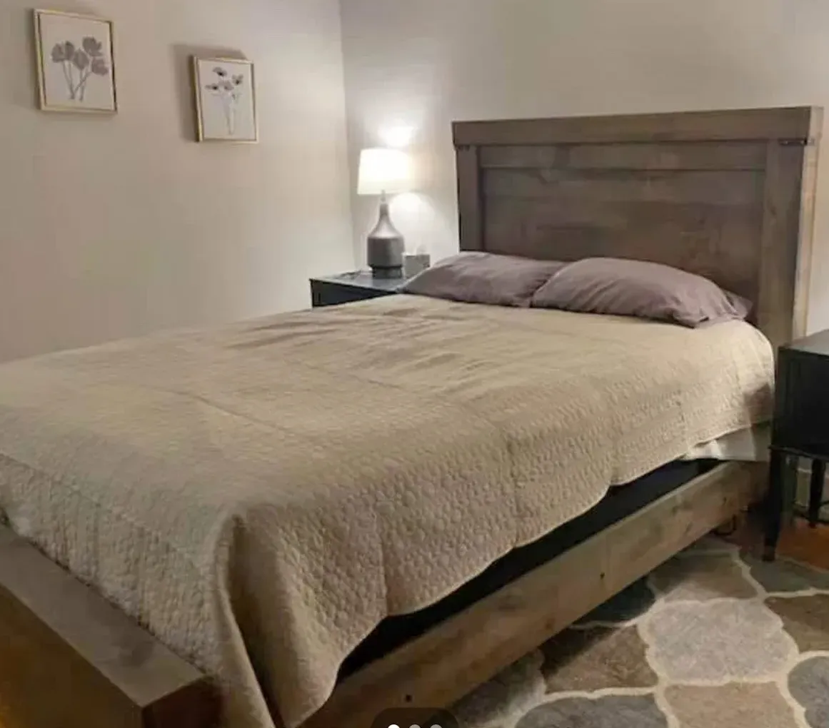 Bedroom with wooden bed frame, headboard, nightstands, and beige bedding. Two framed flower art pieces on wall.