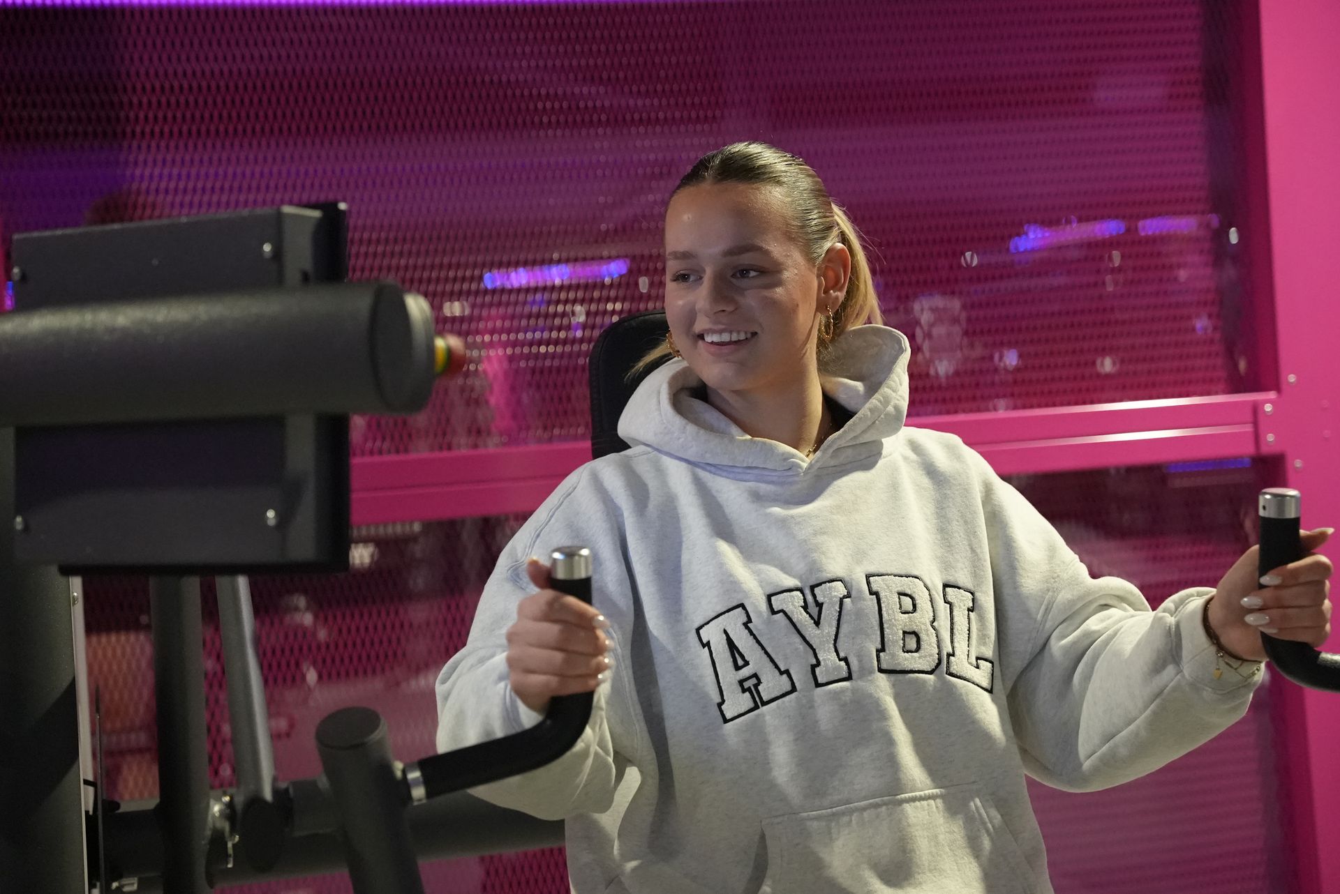 Een vrouw in een hoodie gebruikt een apparaat in een sportschool.