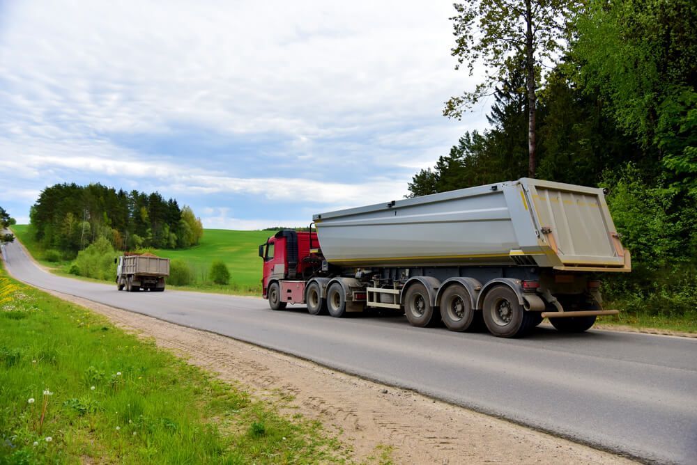 A Dump Truck Is Driving Down A Country Road — Dicko's Bobcat & Tipper in East Bendigo, VIC