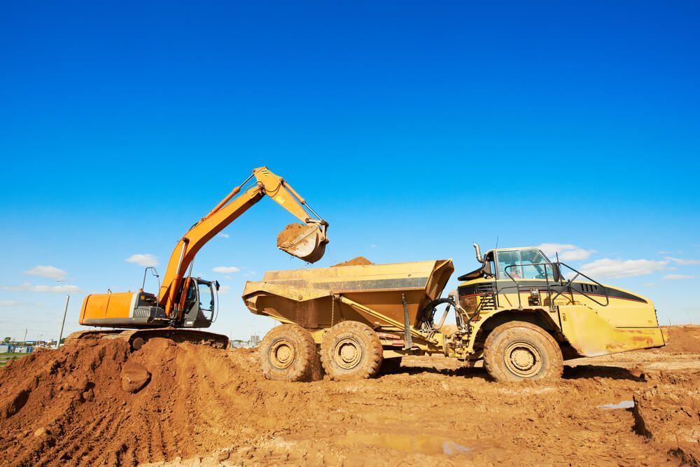 An Excavator Is Loading Dirt Into A Dump Truck At A Construction Site — Dicko's Bobcat & Tipper in East Bendigo, VIC