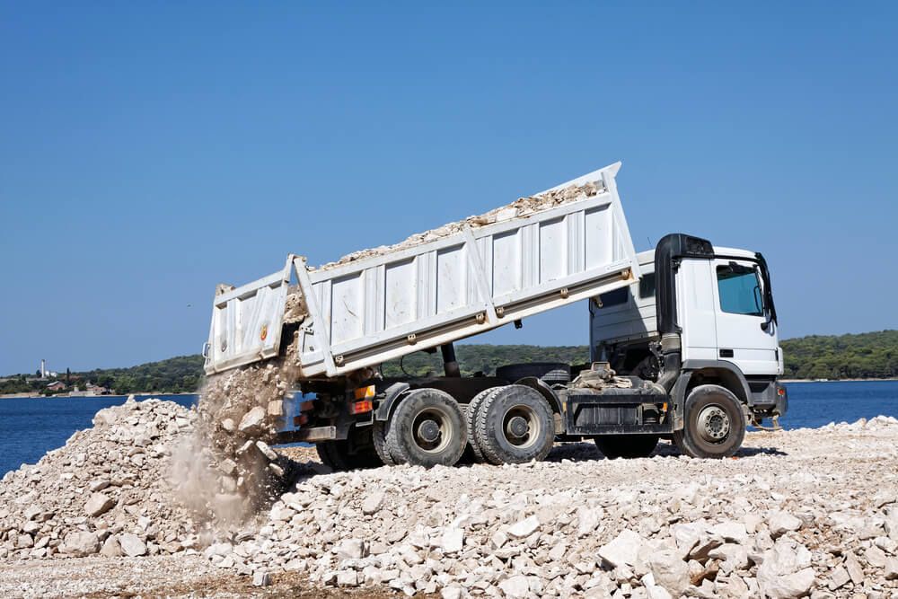 A Dump Truck Is Dumping Rocks Besides A Body Of Water — Dicko's Bobcat & Tipper in East Bendigo, VIC