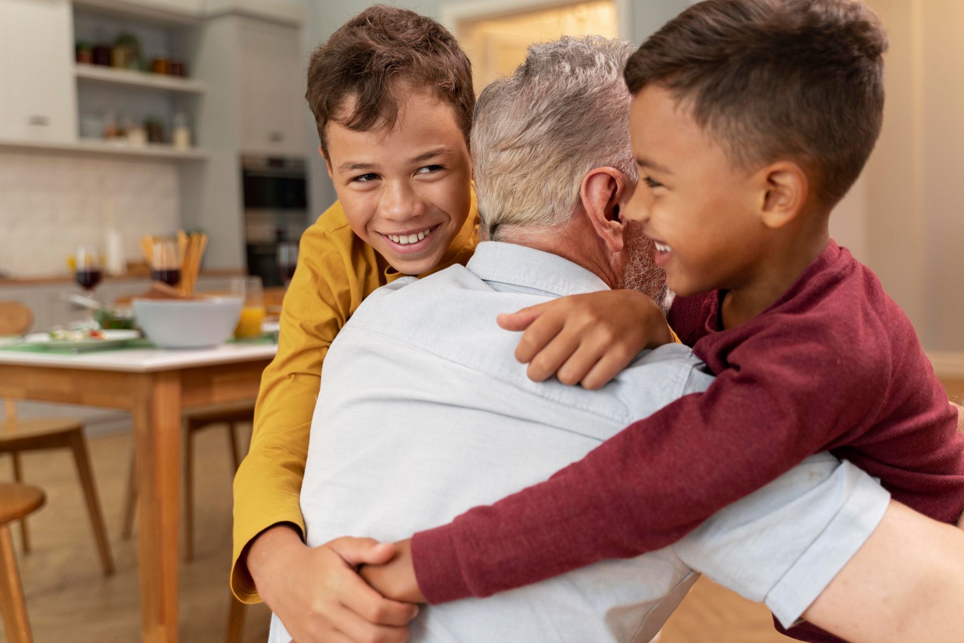 Two children happily embrace an adult in a brightly lit kitchen setting.