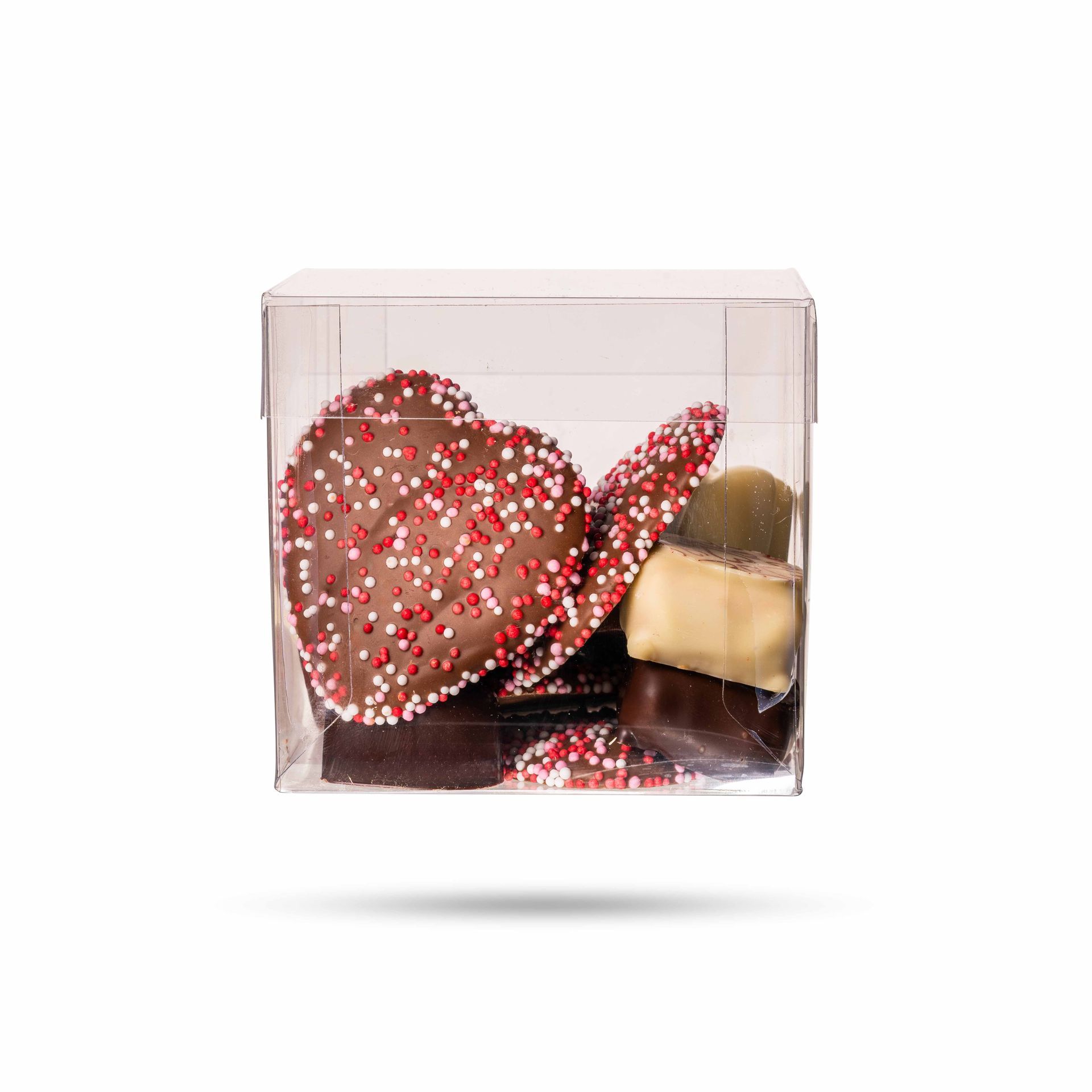 Doorzichtige plastic doos gevuld met diverse chocolaatjes, waaronder hartvormige chocolaatjes met rode en witte sprinkles.
