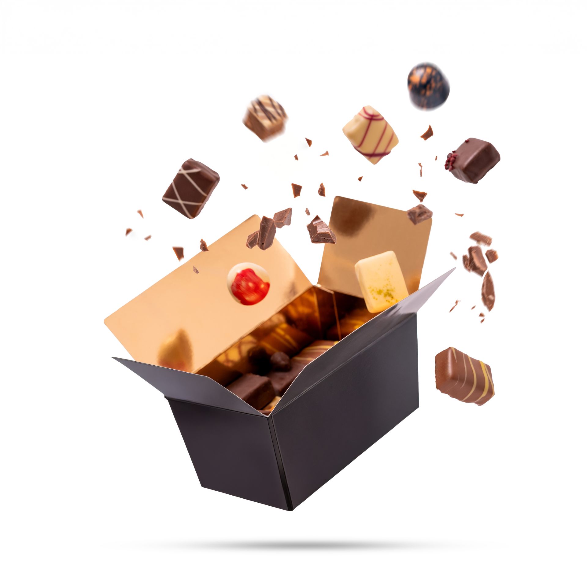 Chocoladedoos explodeert, chocolaatjes vliegen eruit. Zwarte doos met gouden binnenkant en deksel, diverse chocolaatjes in de lucht.