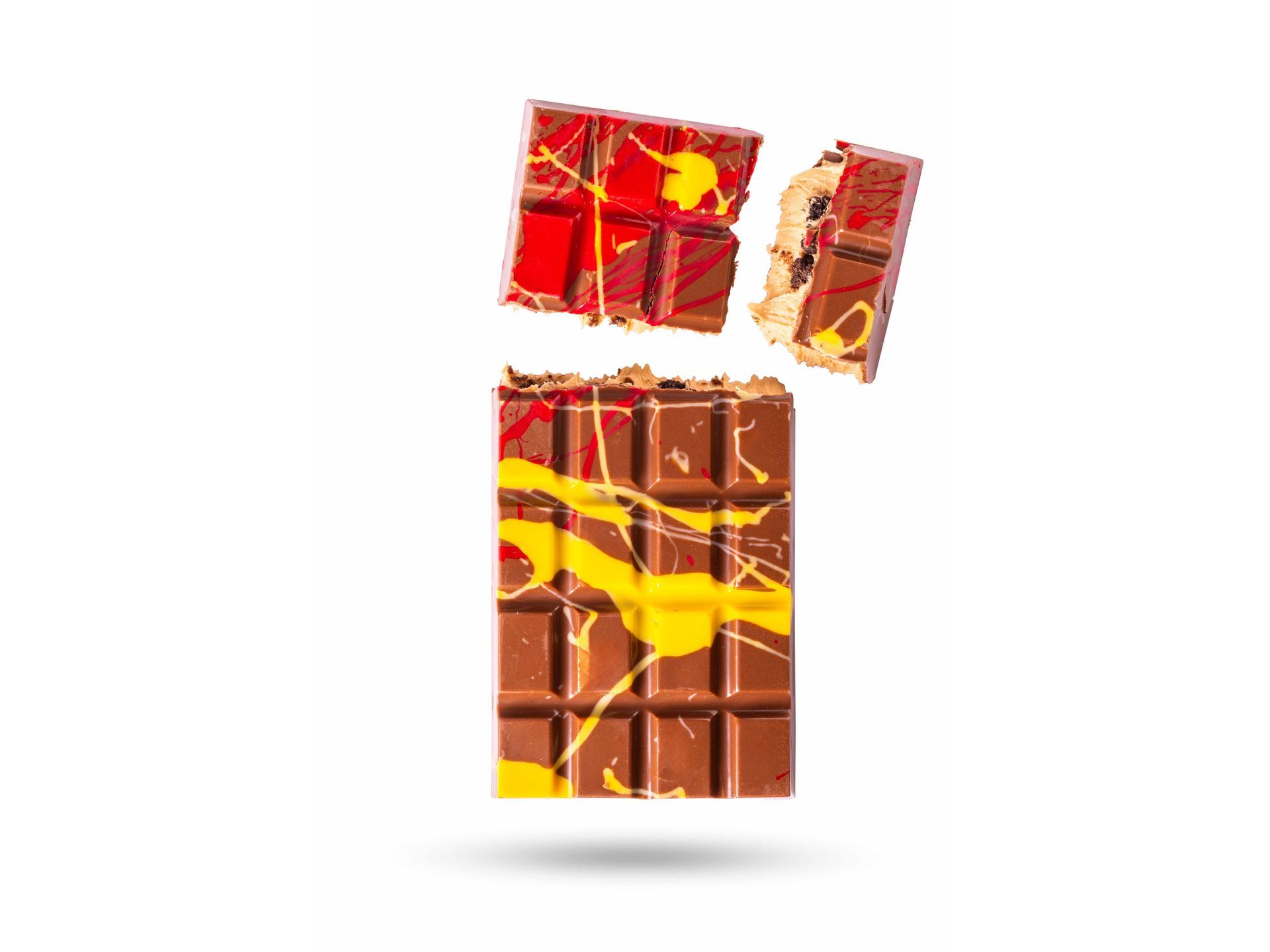 Een chocolade reep met gele en rode verfspatten, in stukken gebroken, zweeft in de lucht.