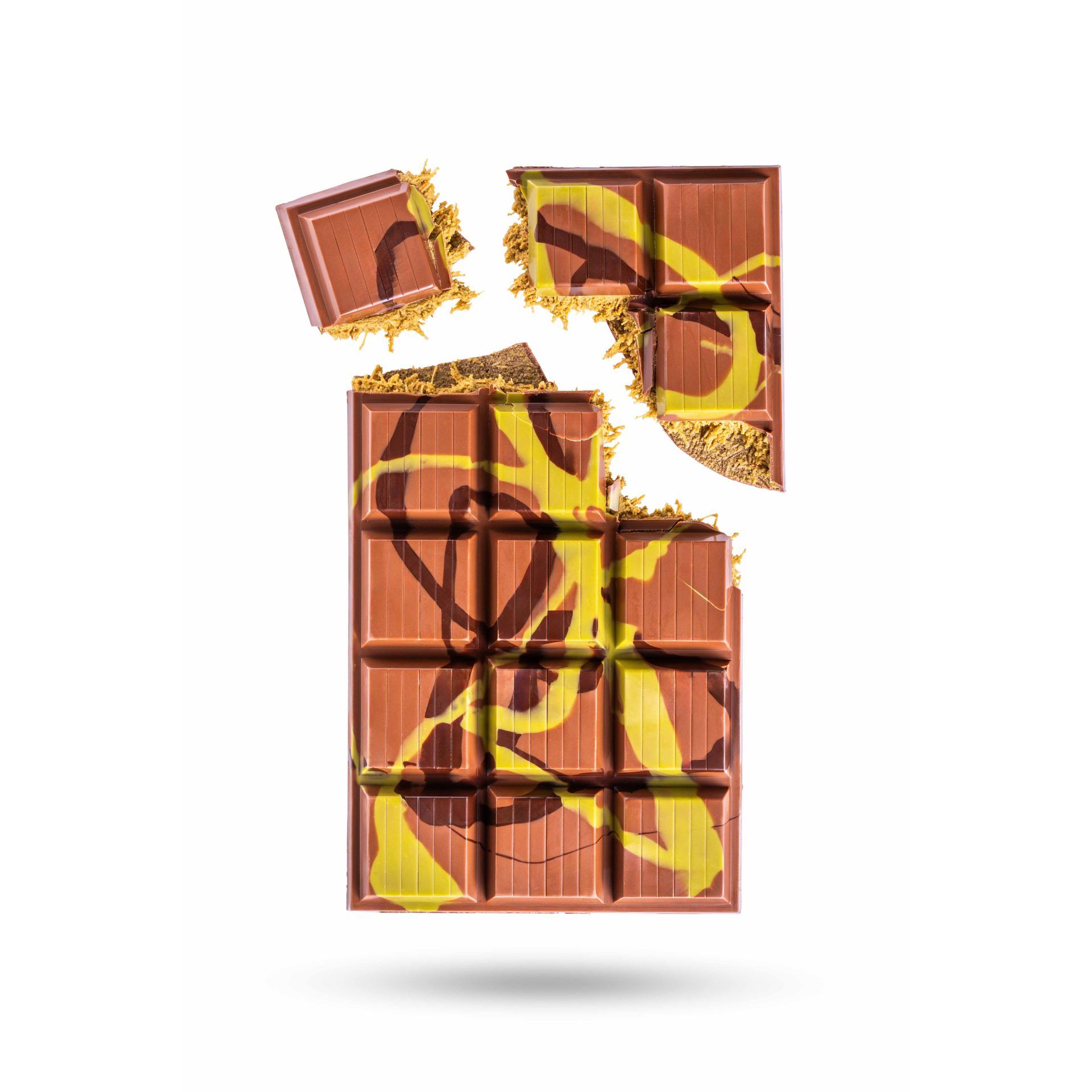 Een gebarsten chocoladereep met gele en bruine spiralen op een witte achtergrond. Kruimels verspreid rond de gebroken stukken.