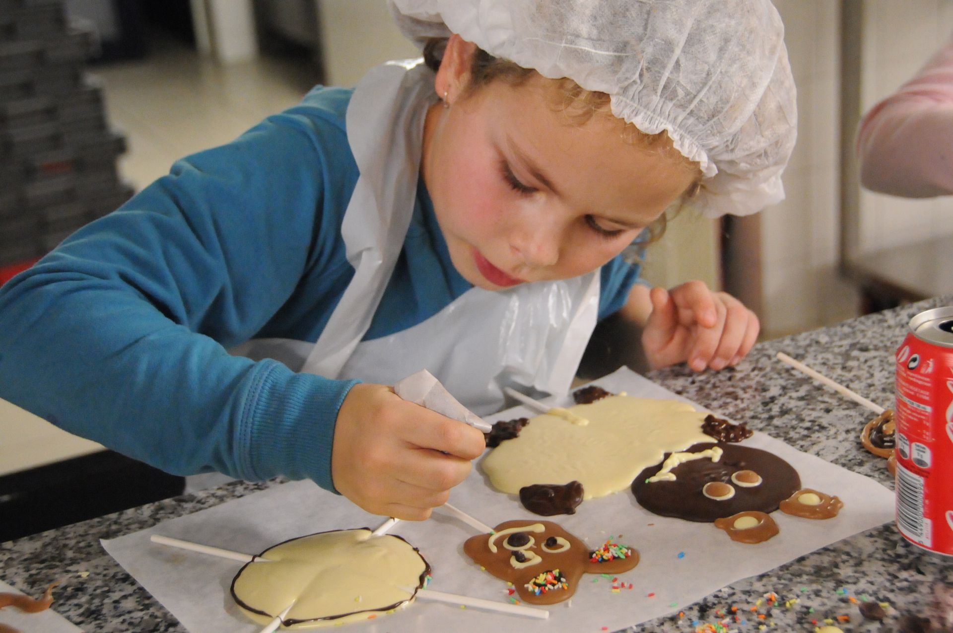 Een jong kind versiert chocoladelolly's in de vorm van dieren met glazuur in een professionele keuken.