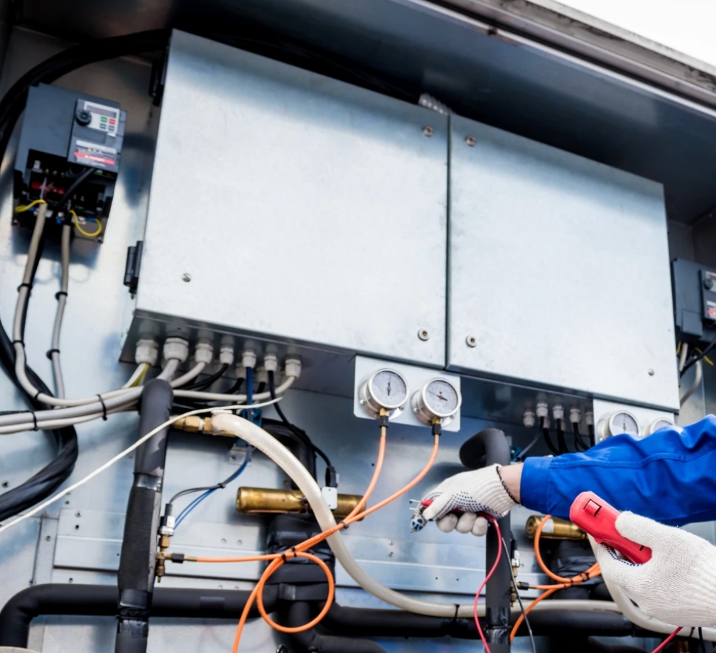 Technician testing electrical control panel with gauges and wires in an industrial setting