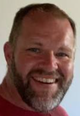 Smiling bearded man in a red shirt, close-up against a light background