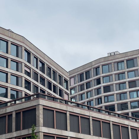 Curved modern office buildings with gray and blue windows under a cloudy sky