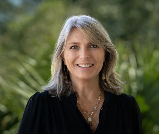 A woman is sitting at a desk with a laptop and a vase of flowers.