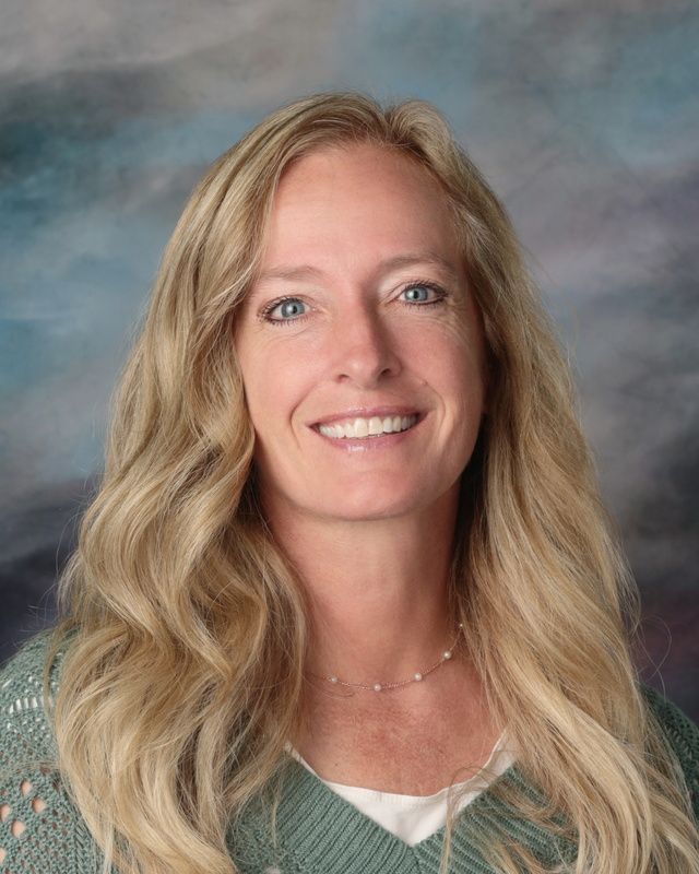 A woman with long blonde hair is smiling for a picture in front of a blue background.