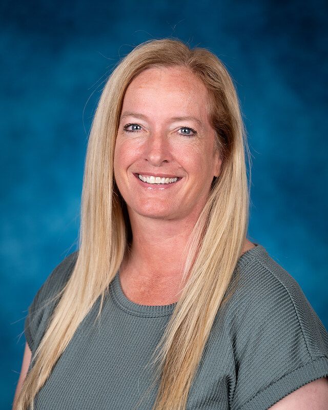 A woman with long blonde hair is smiling for a picture in front of a blue background.