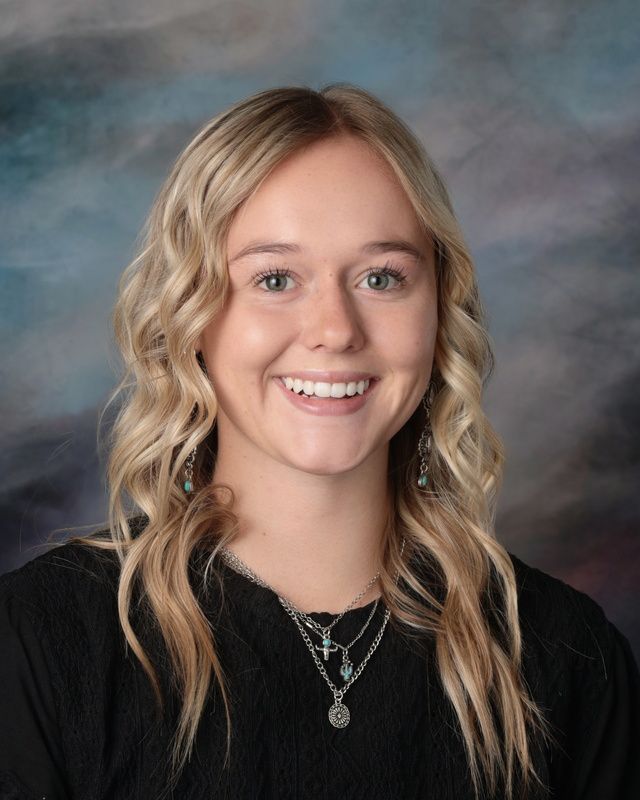 A young woman with long blonde hair is smiling for a picture in front of a blue background.