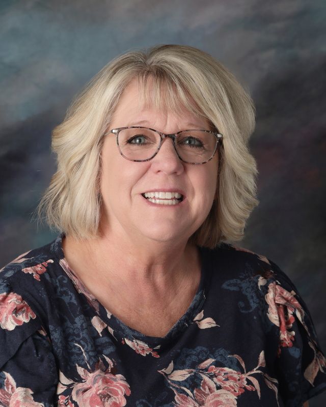 A woman wearing glasses and a gray shirt is smiling for the camera.