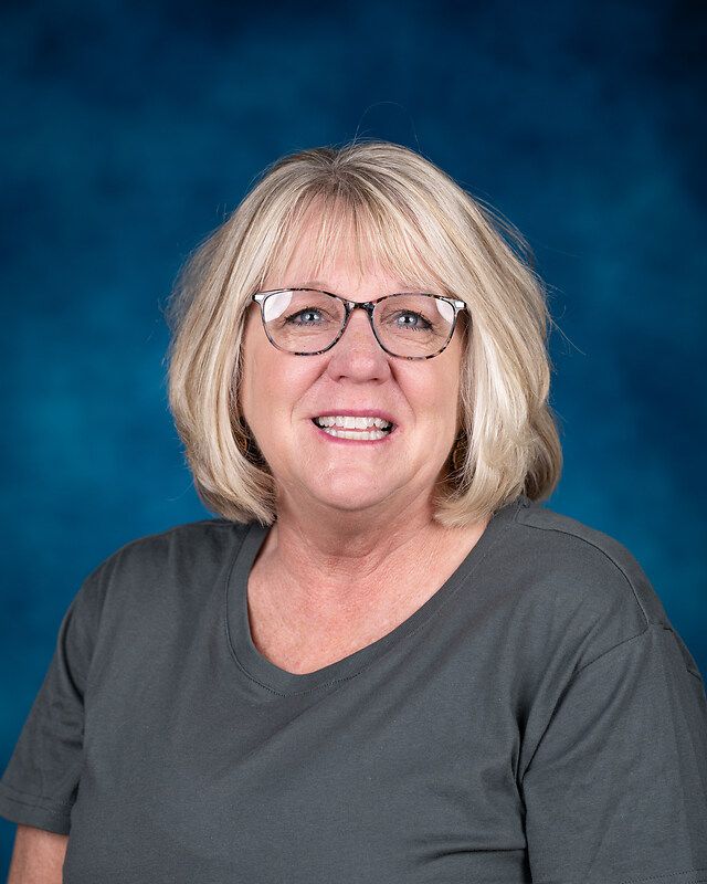 A woman wearing glasses and a gray shirt is smiling for the camera.