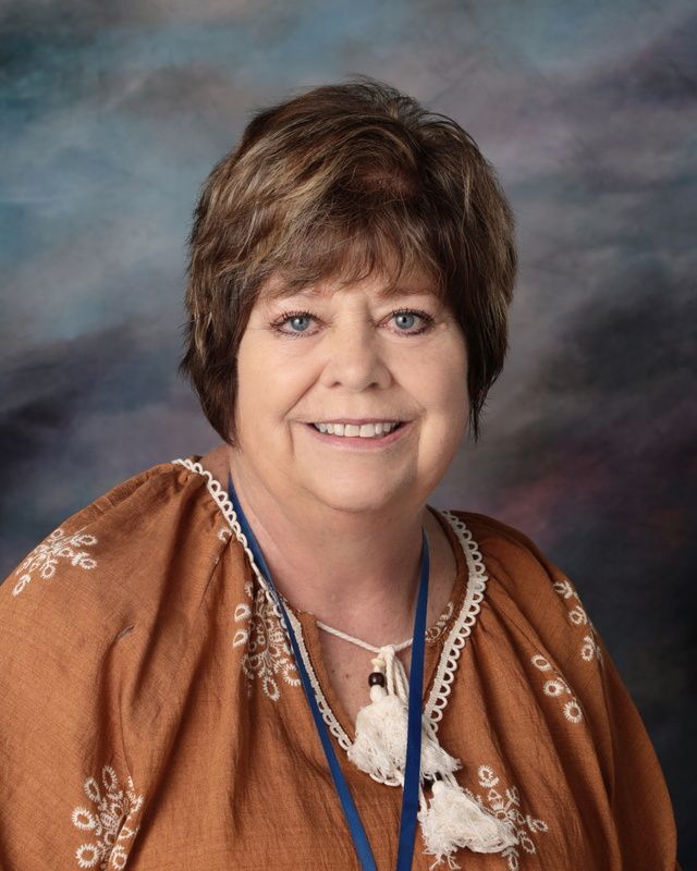 A woman in a black shirt is smiling in front of a blue background.