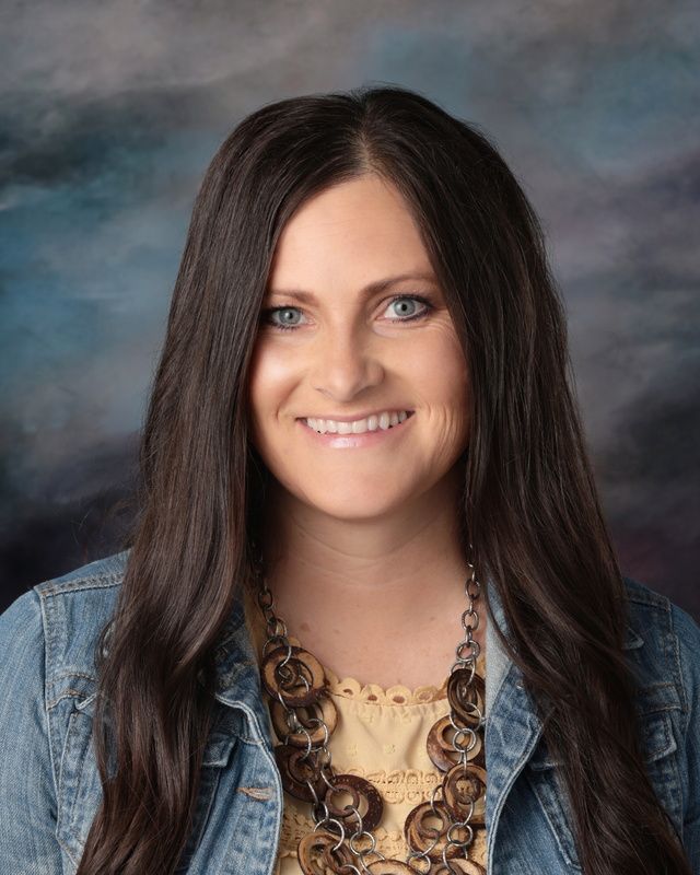 A woman with long hair is wearing a necklace and a blue shirt.