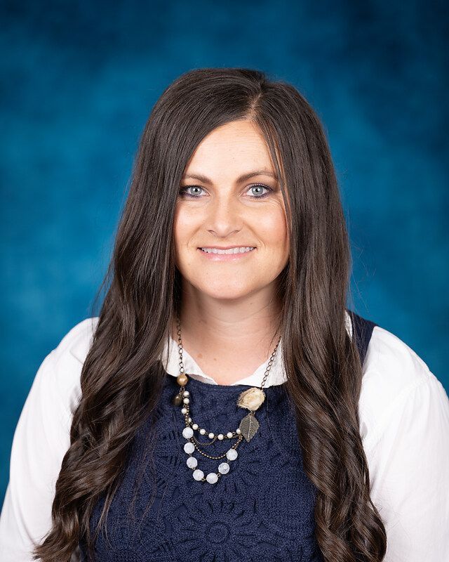 A woman with long hair is wearing a necklace and a blue shirt.