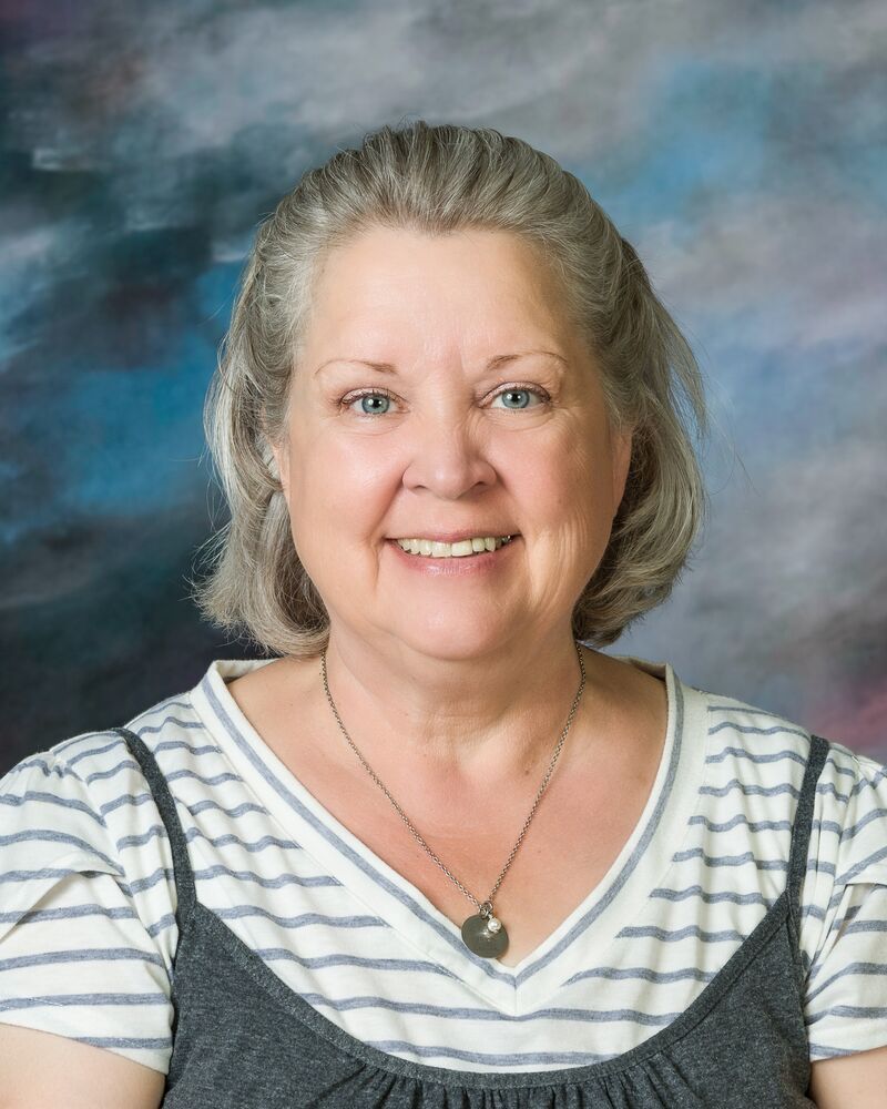 A woman wearing a striped shirt and a necklace is smiling for the camera.