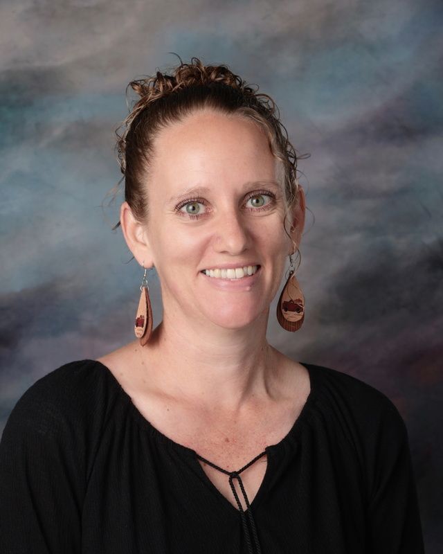 A woman with long curly hair is smiling in front of a blue background.