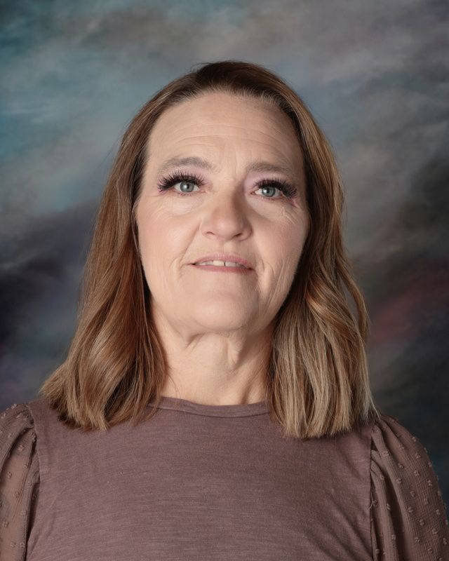 A woman in a floral shirt and necklace is smiling for the camera.