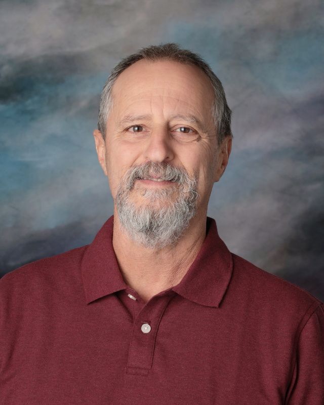 A man with glasses and a beard is standing in front of a blue background.