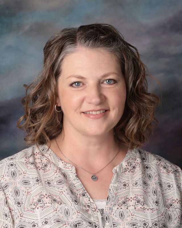 A woman in a floral shirt and necklace is posing for a picture.